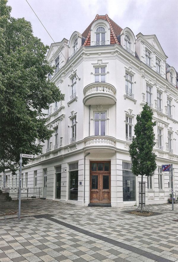 Ein schön saniertes Gründerzeithaus mit runden Balkonen und Bäumen davor
