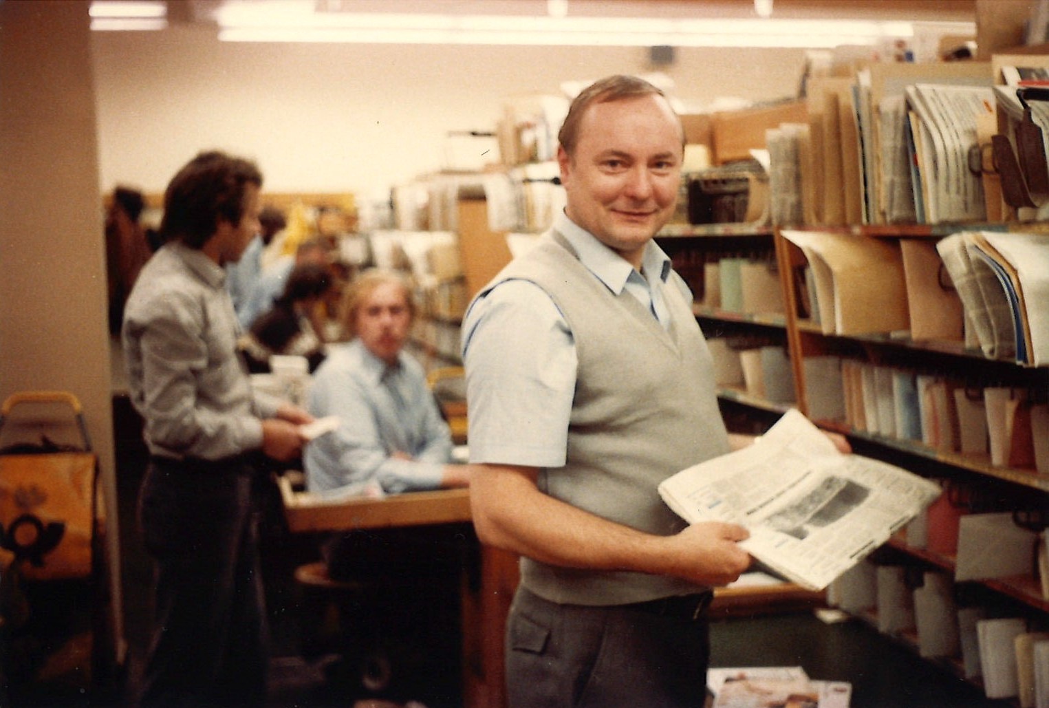 Fredy Troebner mit einer Zeitung in der Hand vor einem Regal mit sortierten Schriftstücken.